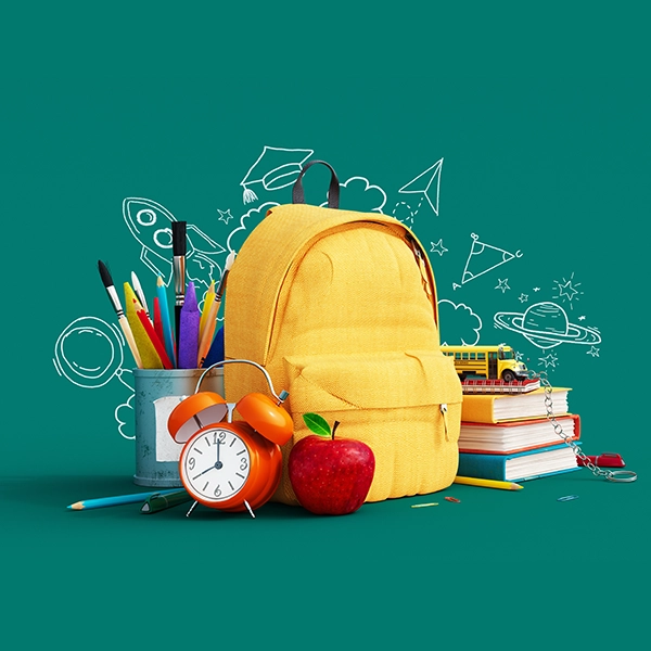 żółty plecak na zielonym tle z przyborami szkolnymi