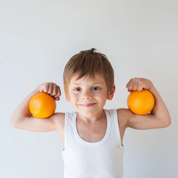 dziecko pokazuje mięśnie i trzyma zdrowe pomarańcze na rękach